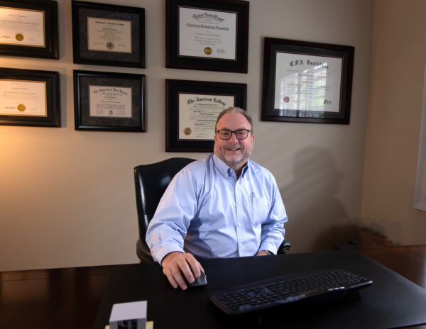 Financial Planner David at his desk with a wall of certificates and diplomas behind him