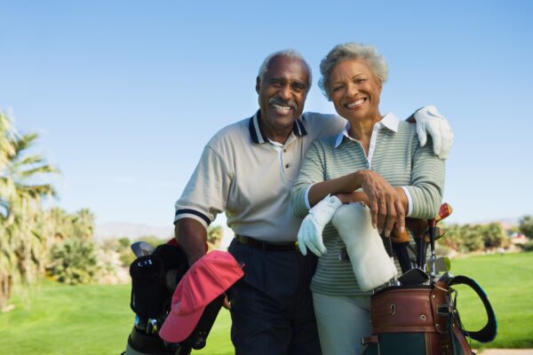 Retired senior couple with golf bags on the course smiling at the camera enjoying the rewards of wealth management