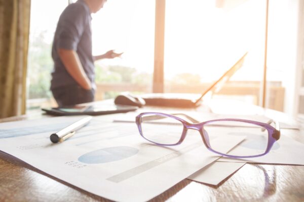 financial planner looking out the window with glasses on a desk in the foreground